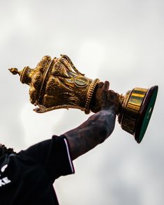 a man holding up a golden trophy in his hand and wearing a black shirt with white lettering on it