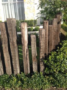 a wooden fence made out of logs in front of a house with bushes around it