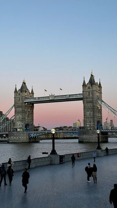 people walking on the sidewalk in front of tower bridge at dusk, london, england