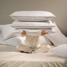 a person sitting on a bed covered in pillows and holding their hands up to the pillow