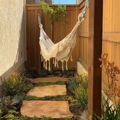 a hammock hanging in the middle of a yard with plants and rocks on either side