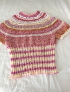 a pink and yellow sweater is laying on a white bed with the words knitted by