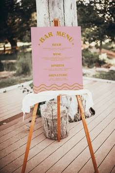 a pink sign sitting on top of a wooden easel next to a white table cloth