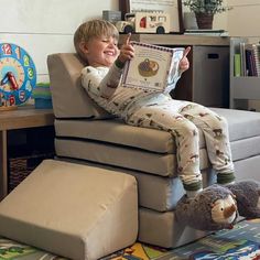 a little boy sitting in a chair reading a book