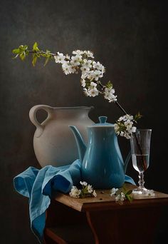 two vases with flowers in them sitting on a table next to a glass cup