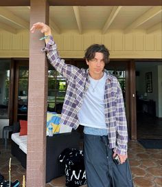 a young man leaning against a pillar with his hand in the air while wearing a plaid jacket