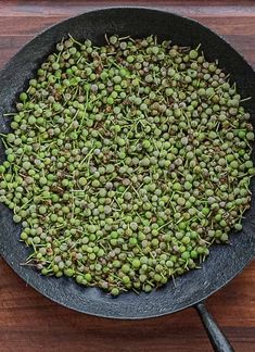 a frying pan filled with green peas on top of a wooden table