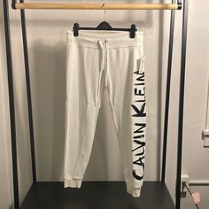 Stylish Black And White Jogger Pants By Calvin Klein White Relaxed Fit Bottoms With Letter Print, Relaxed Fit White Pants With Letter Print, White Fitted Sweatpants, White Stretch Bottoms With Letter Print, Fitted White Bottoms With Letter Print, Calvin Klein Relaxed Fit Summer Bottoms, White Letter Print Bottoms For Loungewear, Calvin Klein Casual Stretch Bottoms, Casual Stretch Calvin Klein Bottoms