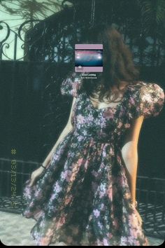 a woman standing in front of a gate wearing a dress with flowers on the back