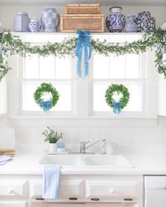 a kitchen with blue and white vases on the window sill, potted plants in front of the sink