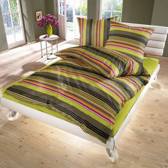 a bed with green and pink striped sheets in a room next to two windows,