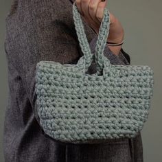 a woman is holding a crocheted handbag in her right hand and looking at the camera