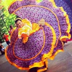 a woman in purple and orange dress holding a large object with her arms out to the side