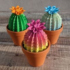 three potted plants with different colored paper flowers in them on a wooden table top