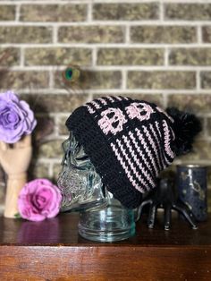 a knitted hat sitting on top of a wooden table next to a vase with flowers