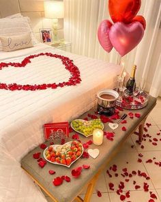 a table topped with lots of food next to a bed covered in red rose petals