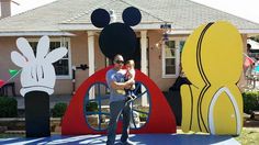 a man holding a baby in front of mickey mouse sculptures