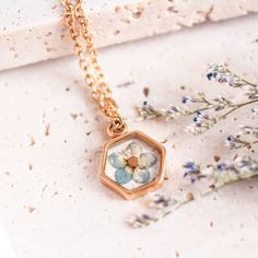 a gold necklace with flowers on it sitting next to a flower pot and some plants