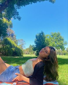 a beautiful young woman laying on top of a blanket in the grass next to a tree