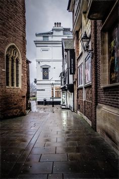 an alley way with brick buildings and cobblestone pavement in the foreground, on a rainy day