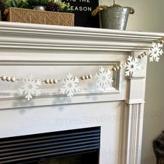 a white fireplace with snowflakes hanging from it's mantle and decorations on the mantel