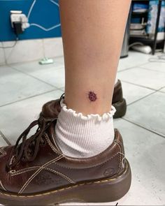 a woman's foot with a tiny flower tattoo on her left ankle, and a pair of brown shoes