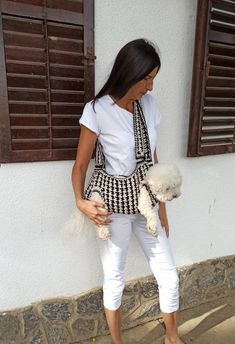 a woman holding a white poodle standing next to a wall with shutters on it