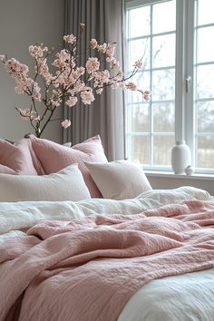 a bed with pink linens and pillows in front of a large window filled with flowers