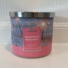 a pink candle that is sitting on a table next to a white tile wall with the words passion fruit beach party written in it