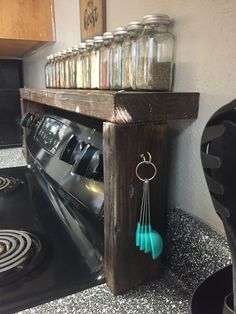 there is a shelf with jars and spoons on it next to the stove top