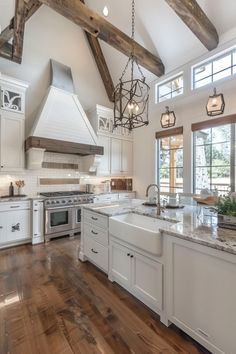 a large kitchen with white cabinets and wood flooring is pictured in this image, there are two chandeliers hanging from the ceiling