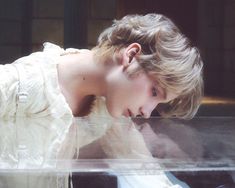 a woman in white dress leaning over a glass case with her hand on the ground