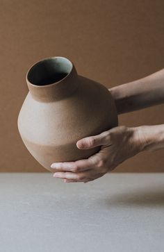 a person is holding a clay vase in their hand and touching it with both hands