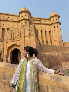 a woman leaning against a wall in front of a castle