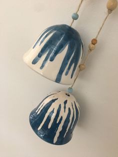 two blue and white vases hanging on a wall with beaded necklaces around them