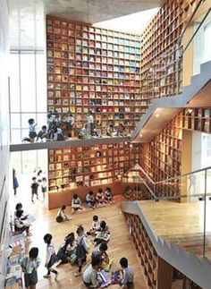 people are sitting on the floor in front of many bookshelves and staircases