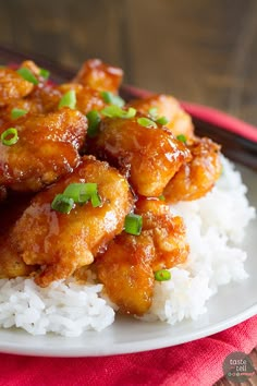 a white plate topped with chicken and rice next to chopsticks on a table