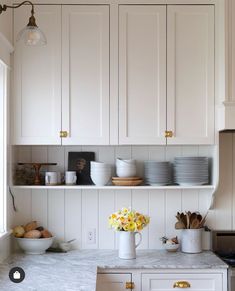 a kitchen with white cabinets and marble counter tops, yellow flowers in a vase on the shelf