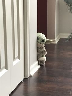 a baby yoda doll peeking out from behind a wall in front of a door