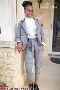 a woman standing next to a brick wall wearing a suit and tie, with her hands on her hips