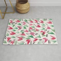 a white rug with pink, green and red leaves on it next to a basket