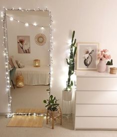 a bedroom with white furniture and string lights on the wall, along with a large mirror