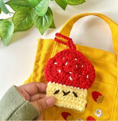 a hand holding a crocheted piece of food in front of a yellow bag