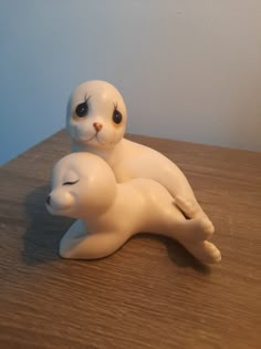 two small white plastic animals sitting on top of a wooden table next to each other