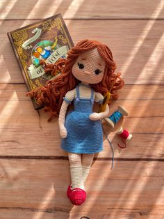 a knitted doll laying on top of a wooden floor next to an open book