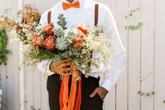 a man wearing an orange bow tie holding a bouquet