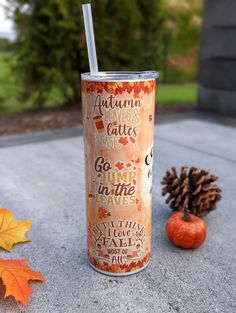 an autumn drink is sitting on the ground next to some leaves and a pine cone