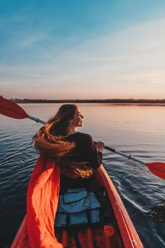 a woman in a red kayak paddling on the water at sunset with her long hair blowing back