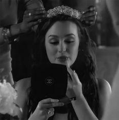 a woman looking at her cell phone while wearing a tiara and holding it in front of her face