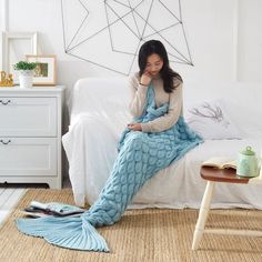 a woman sitting on top of a bed covered in a blue mermaid tail blanket